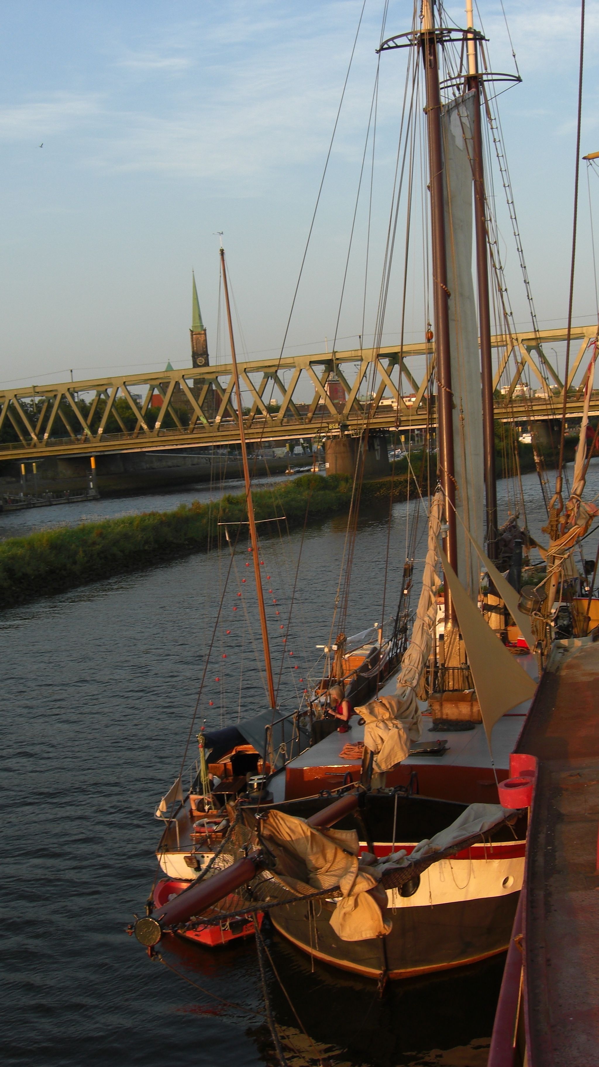 A river with boats docked, a bridge in the background, and a building with a green roof.