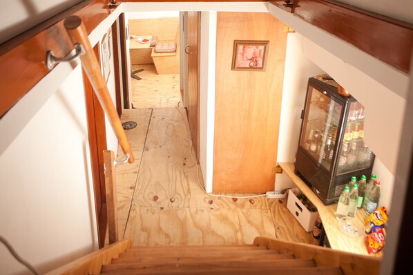 A narrow hallway with wooden flooring leading to a room with a wooden door and a small table with items on it.