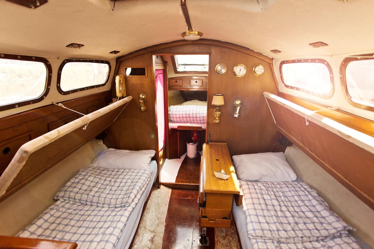 A narrow cabin with two beds, a small table, and a window.