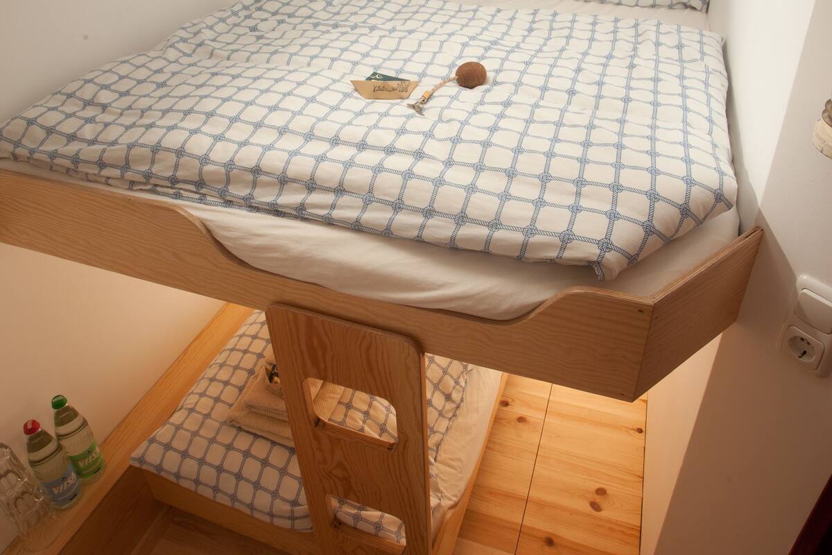 A small, compact room with a bunk bed, wooden flooring, and a small desk area.
