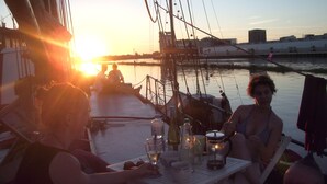 A sunset scene on a boat with people sitting at a table with drinks and glasses. - Klabauterbett (Bremen)