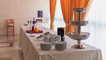 Une table à manger dressée avec des assiettes, des tasses et un distributeur de boissons, avec un panier en métal et une chaise en arrière-plan.