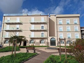 Un edificio residencial de varios pisos con balcones, un patio central con bancos y una pequeña fuente.