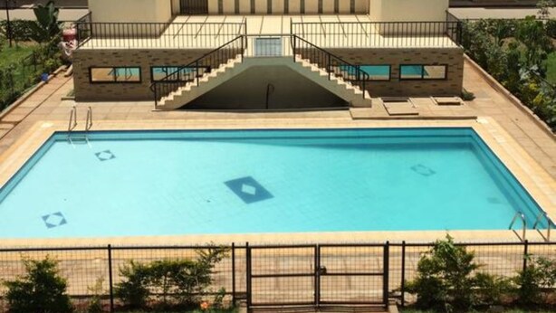 A multi-story building with a central courtyard featuring a swimming pool, surrounded by a fence and greenery. - Jambo Homestay (Syokimau)