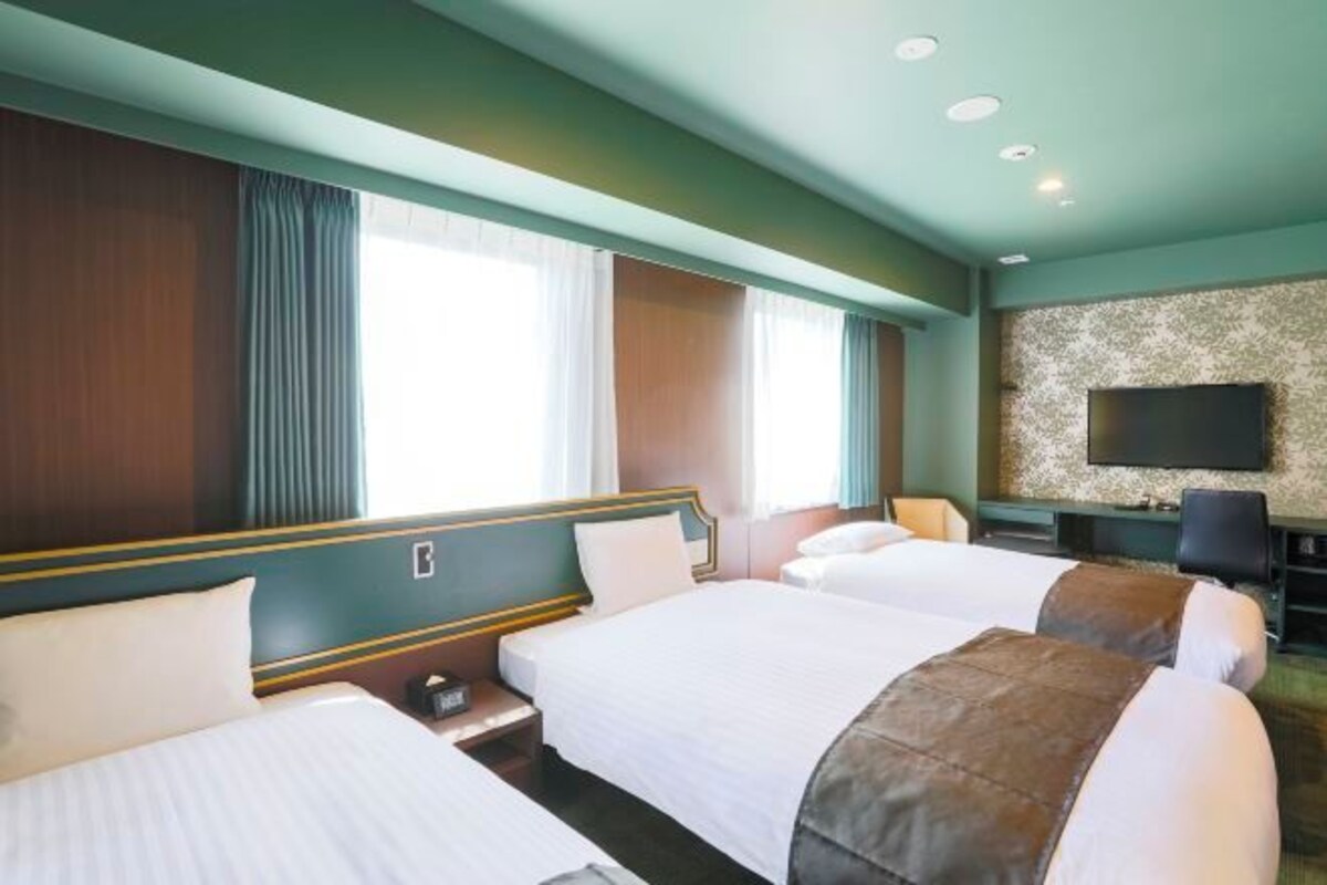 A hotel room with two beds, a flat-screen TV, and a large window with curtains.