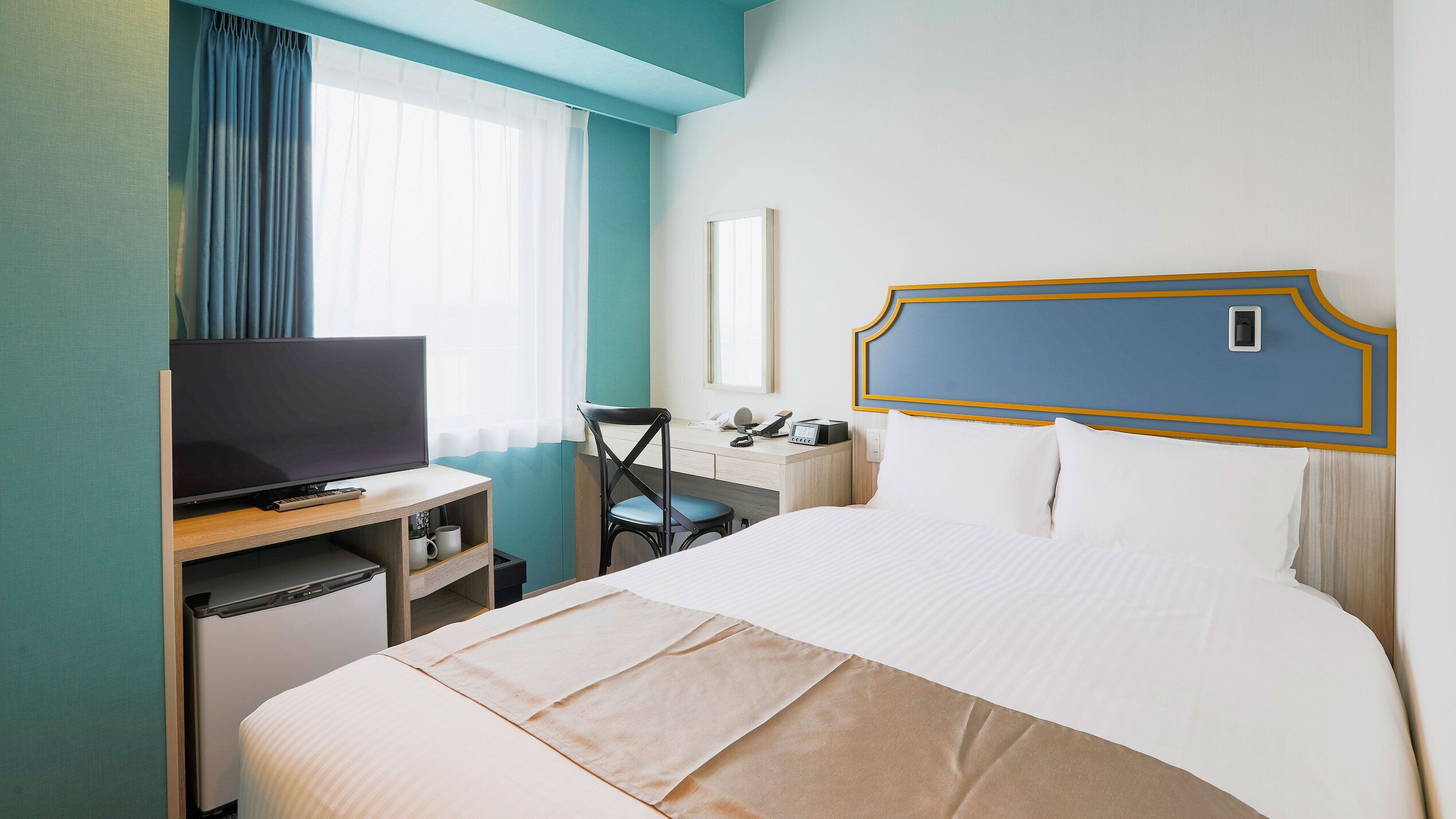 A hotel room with a bed, a desk, a television, a chair, and a window with curtains.