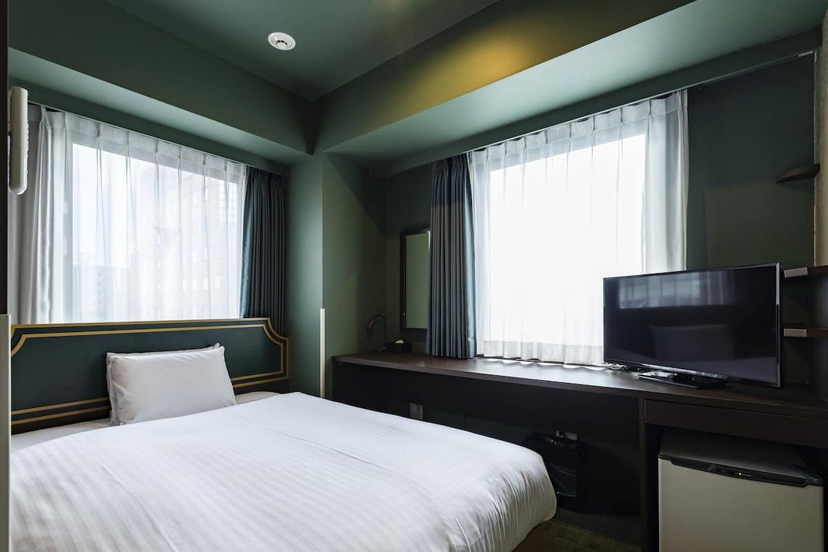 Hotellihuone, jossa on sänky, työpöytä, televisio ja pieni jääkaappi.