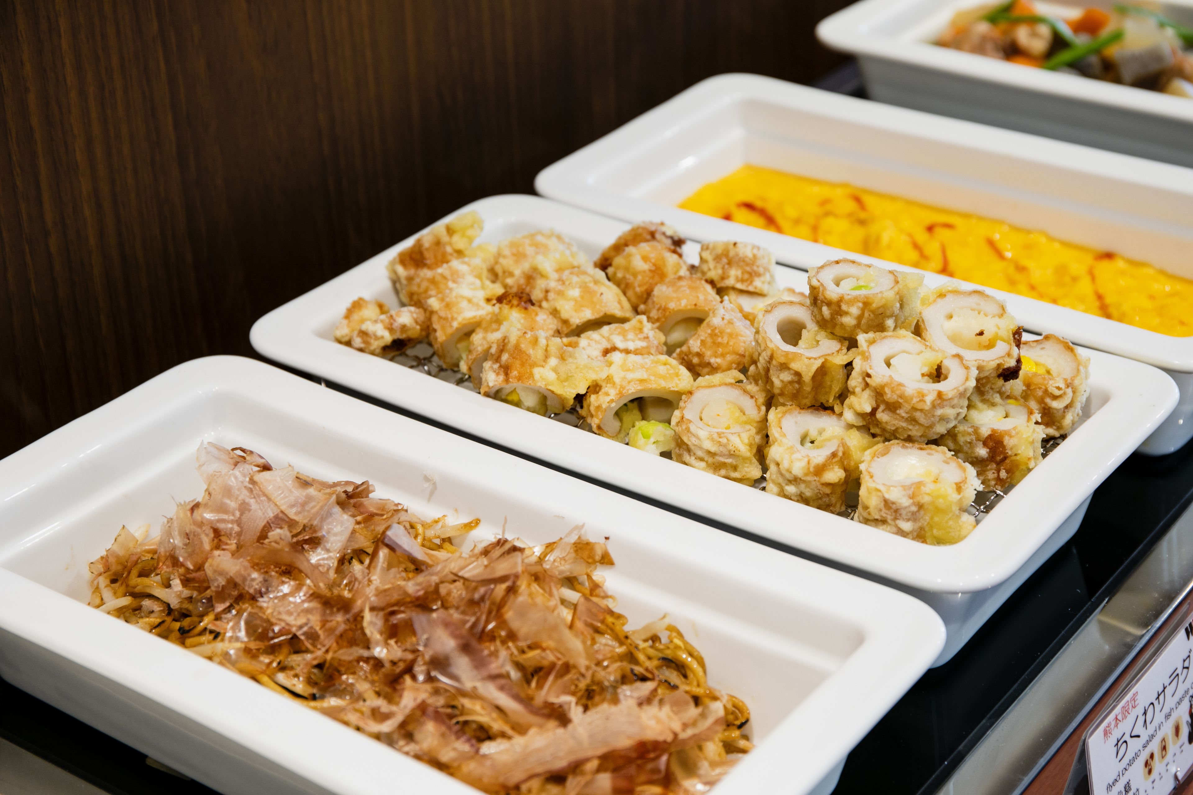 A buffet with various dishes including tempura, sushi, and a yellow rice dish.