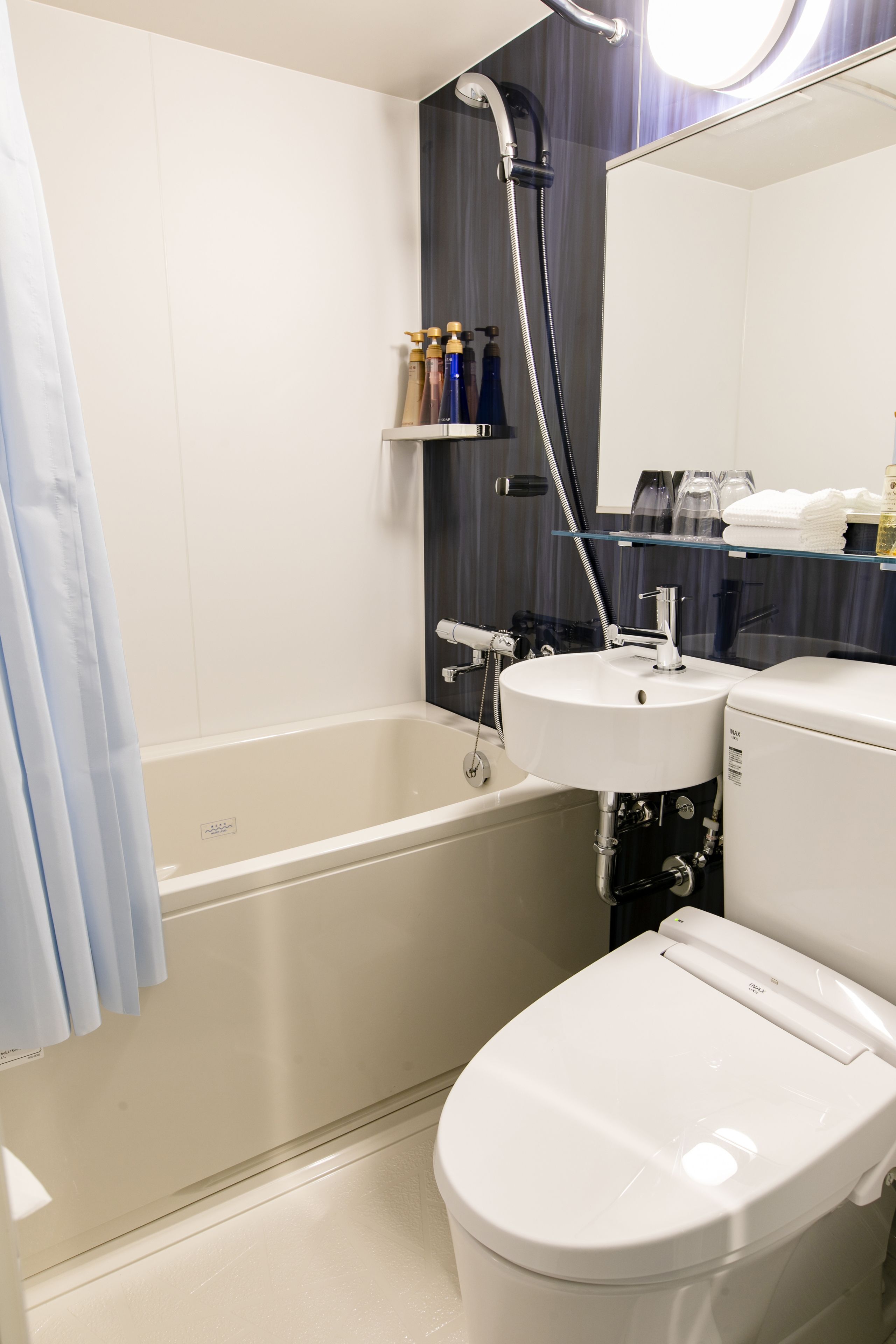 Une salle de bain moderne avec une baignoire, un lavabo et des toilettes. Il y a une pomme de douche au-dessus du lavabo et un miroir au-dessus des toilettes.