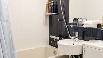 Une salle de bain moderne avec une baignoire, un lavabo et des toilettes. Il y a une pomme de douche au-dessus du lavabo et un miroir au-dessus des toilettes.