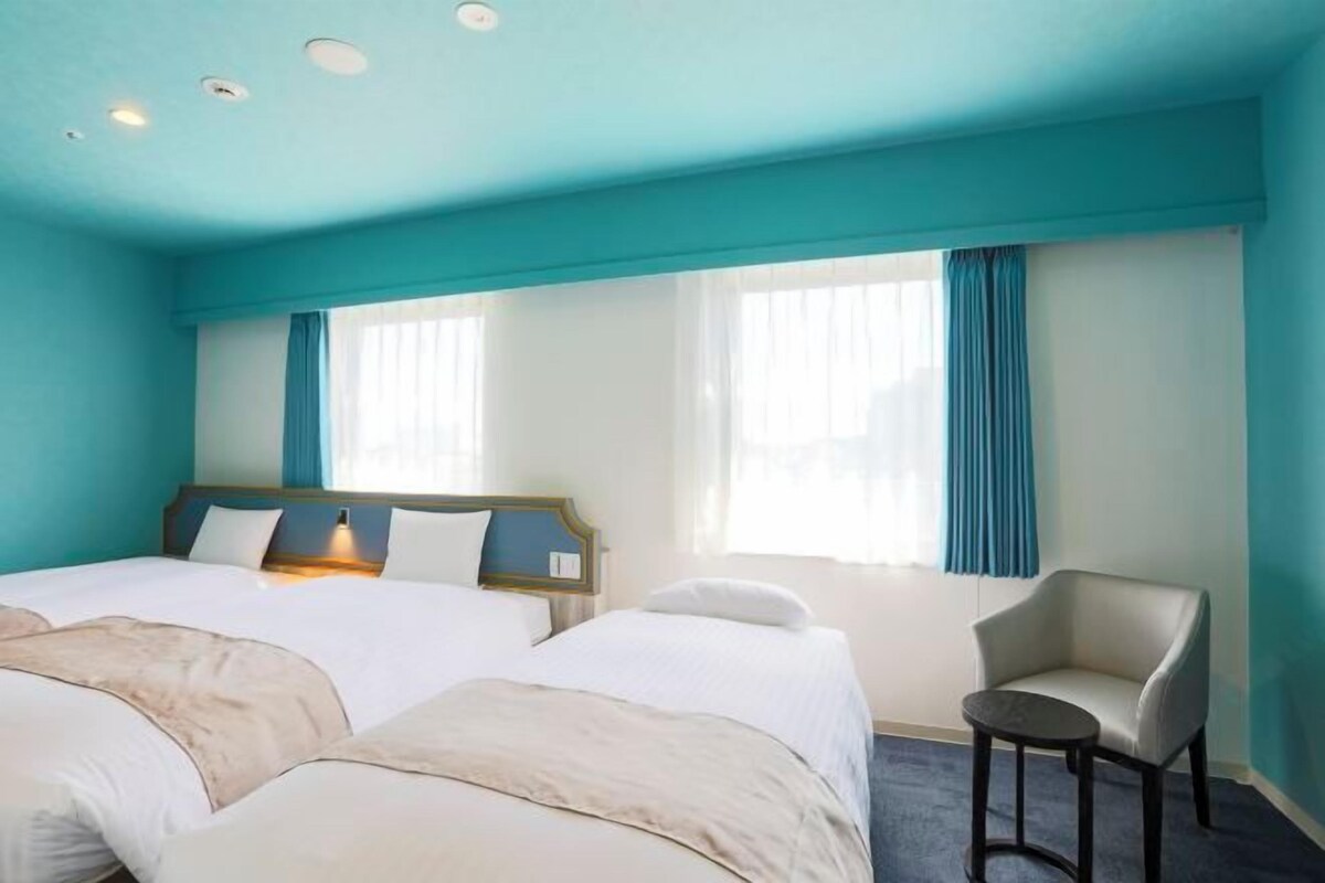 Une chambre d’hôtel avec deux lits, une chaise et de grandes fenêtres avec des rideaux.