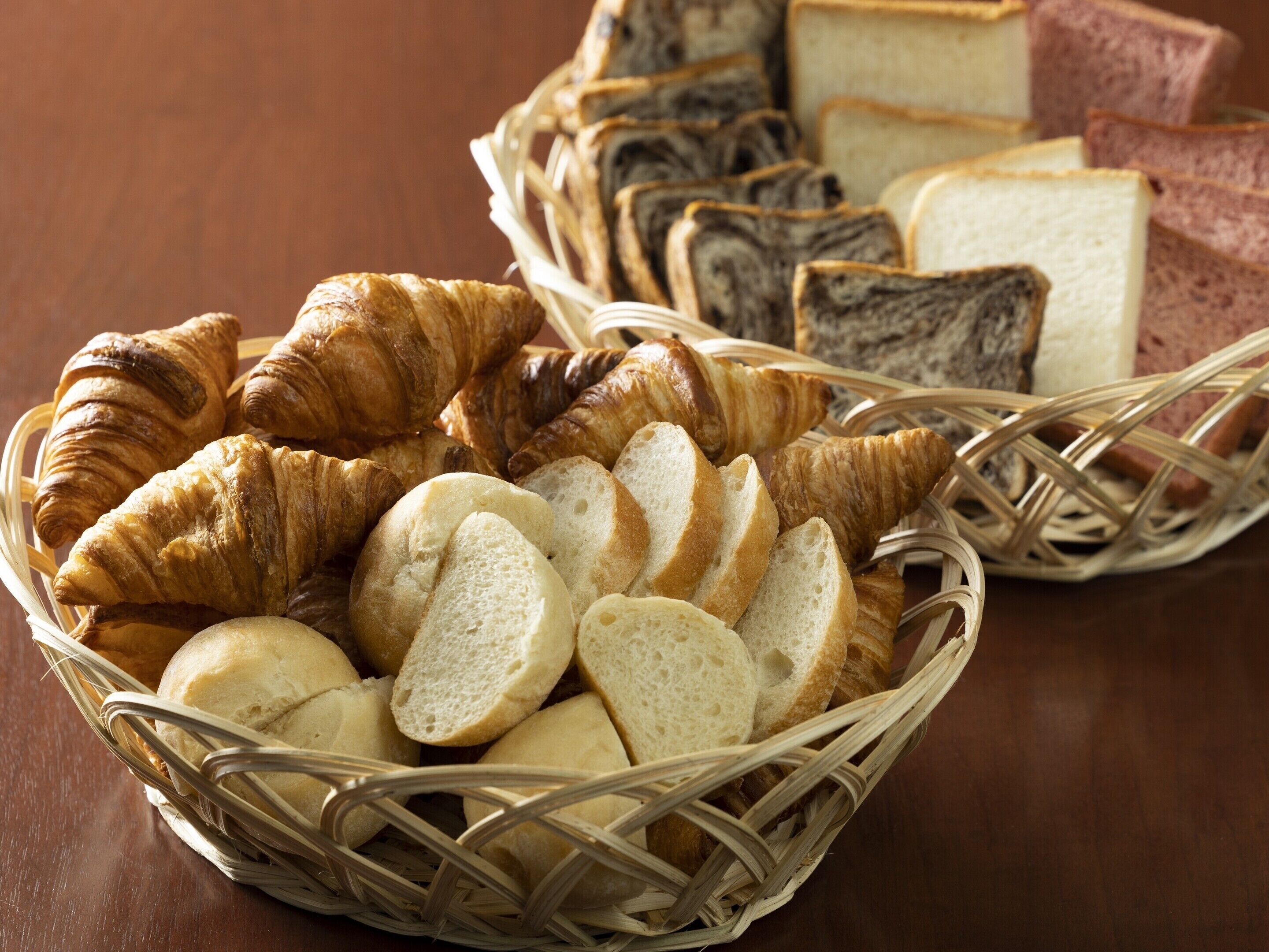 Un panier rempli de pain et de viennoiseries, notamment des croissants et du pain tranché, est posé sur une table en bois.