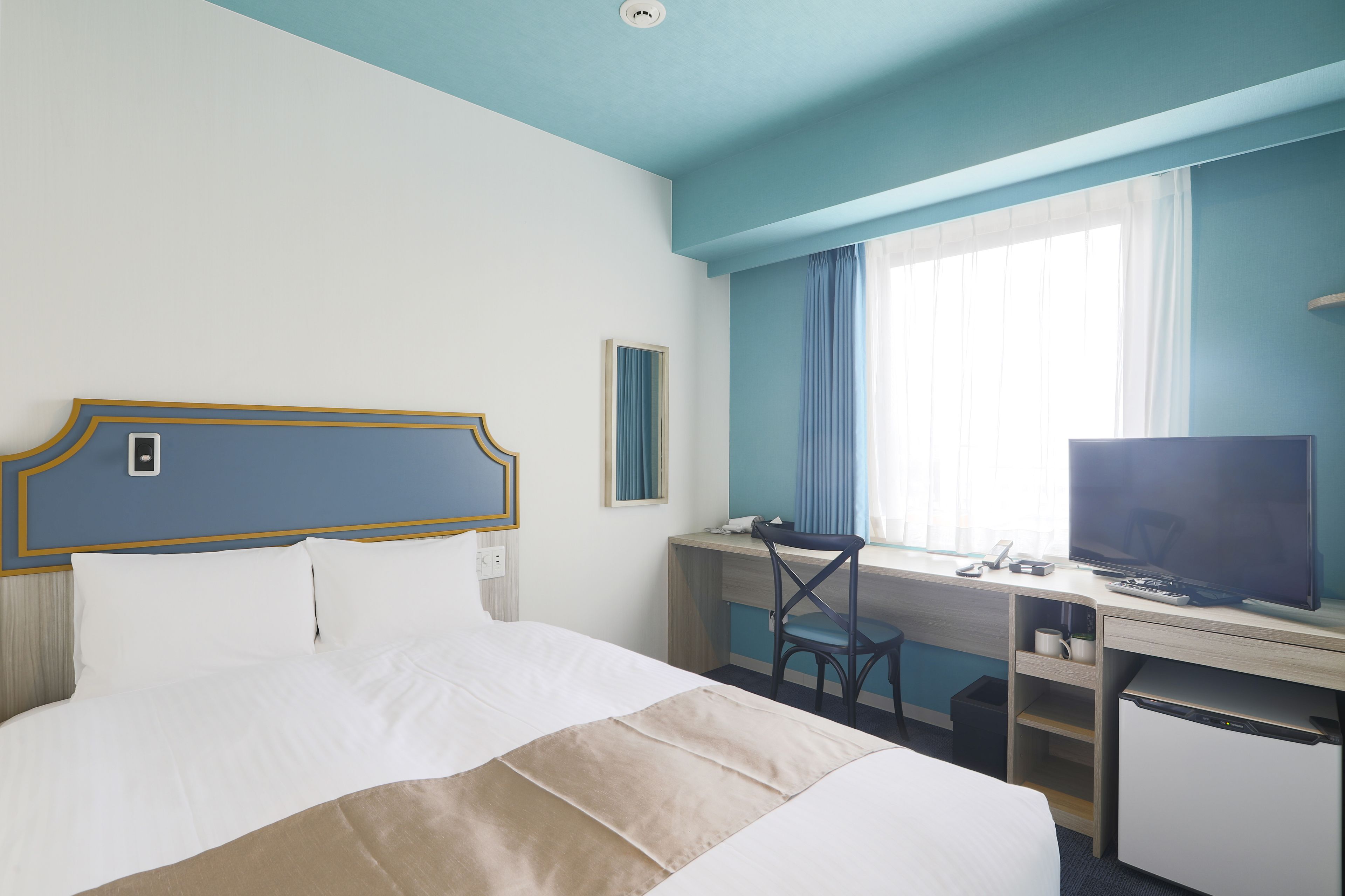 A hotel room with a bed, desk, television, and a window with curtains.