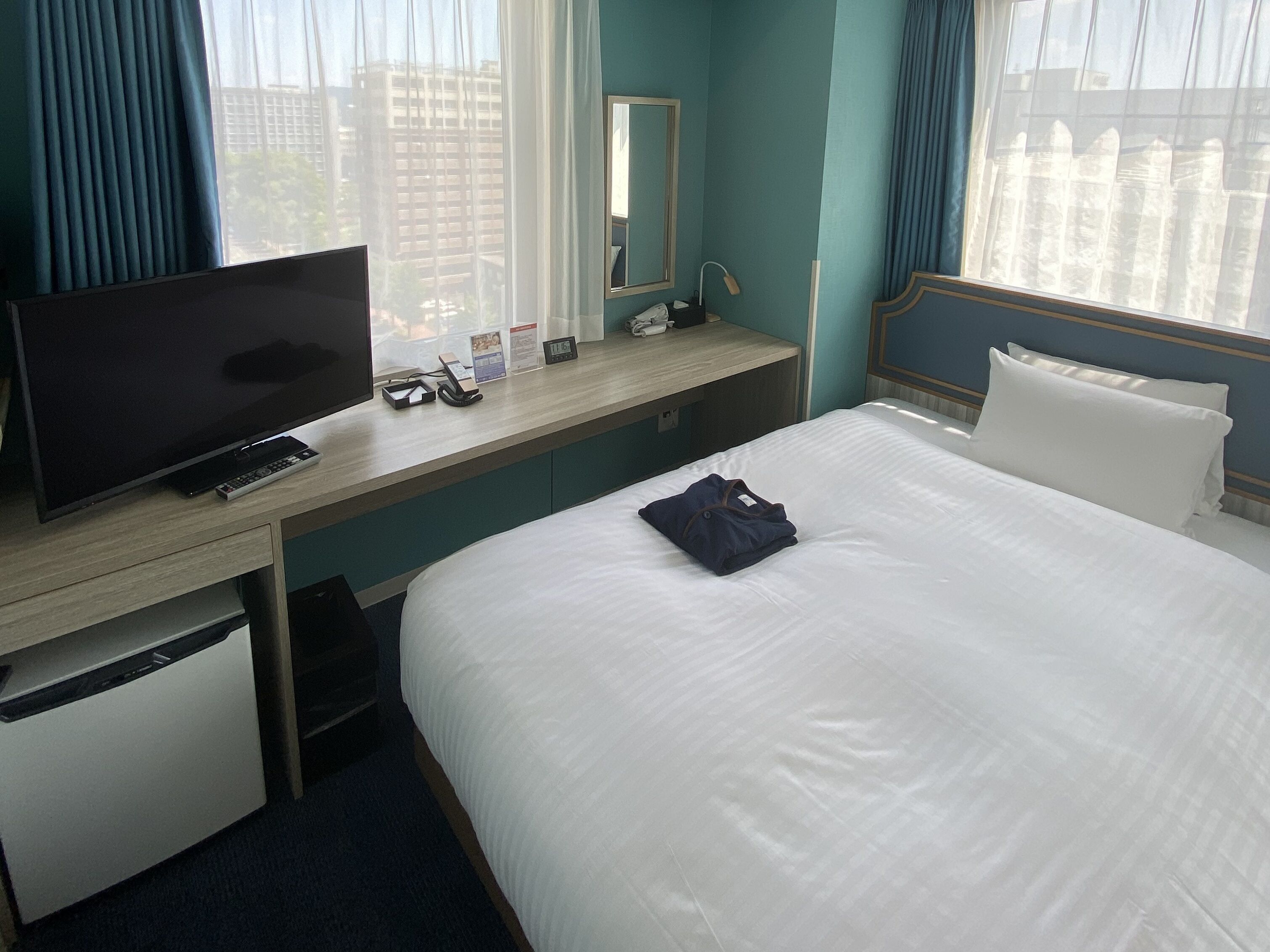 Una habitación de hotel con cama, escritorio con televisor, teléfono y espejo.
