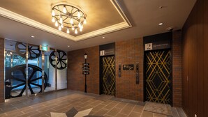 Eine Hotelhalle mit modernem Design, inklusive einem geometrischen Bodenmuster, einer Chandelüster und zwei Aufzügen mit nummerierten Türen.
