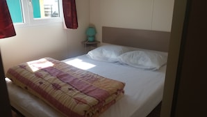 A neatly made bed with a patterned blanket, a bedside lamp, and a window with curtains.