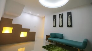 A modern interior with a staircase, a teal sofa, and three wall-mounted artworks. - Return Home B&B (Yuli)