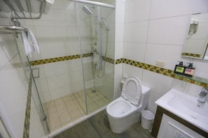 A bathroom with a glass-enclosed shower, a toilet, and a sink. - Return Home B&B (Yuli)
