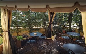 An outdoor patio with tables and chairs, surrounded by potted plants and trees. - B&B Fine Venice (Mestre)