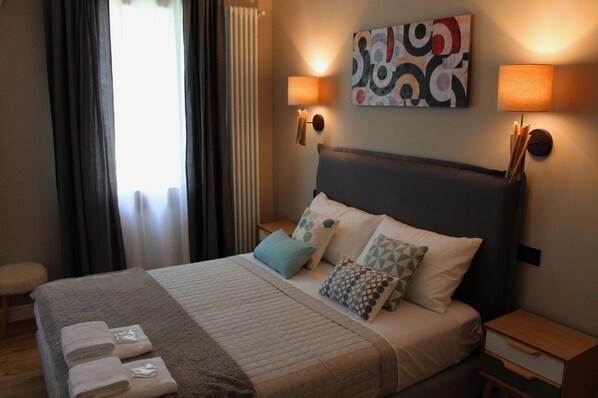 A neatly made bed with a grey headboard, multiple pillows, and a bedside table with a lamp. - B&B Fine Venice (Mestre)