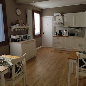 A compact kitchen with white cabinets, a microwave, a coffee maker, and a dining area with a table and chairs. - B&B Fine Venice (Mestre)