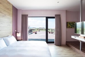 Una habitación de hotel con una cama grande, un escritorio con televisor y un balcón con mobiliario exterior.
