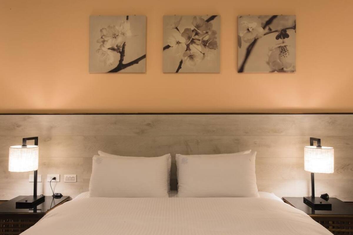 A hotel room with a large bed, two bedside tables with lamps, and three wall-mounted floral artwork.