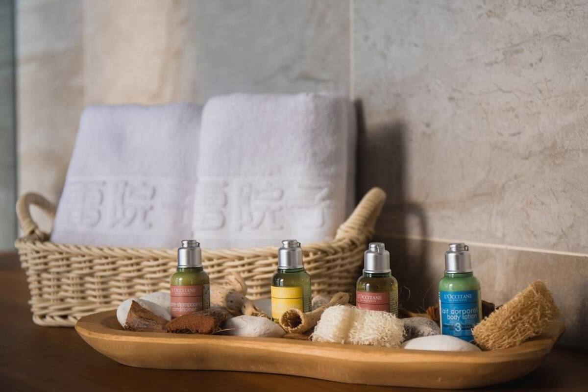 A wooden tray with various toiletries including bottles of lotion and a sponge, placed on a table with a wicker basket and folded towels in the background.