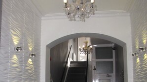 Un couloir orné d’un lustre, avec un escalier et une porte dont les panneaux sont en verre dépoli.
