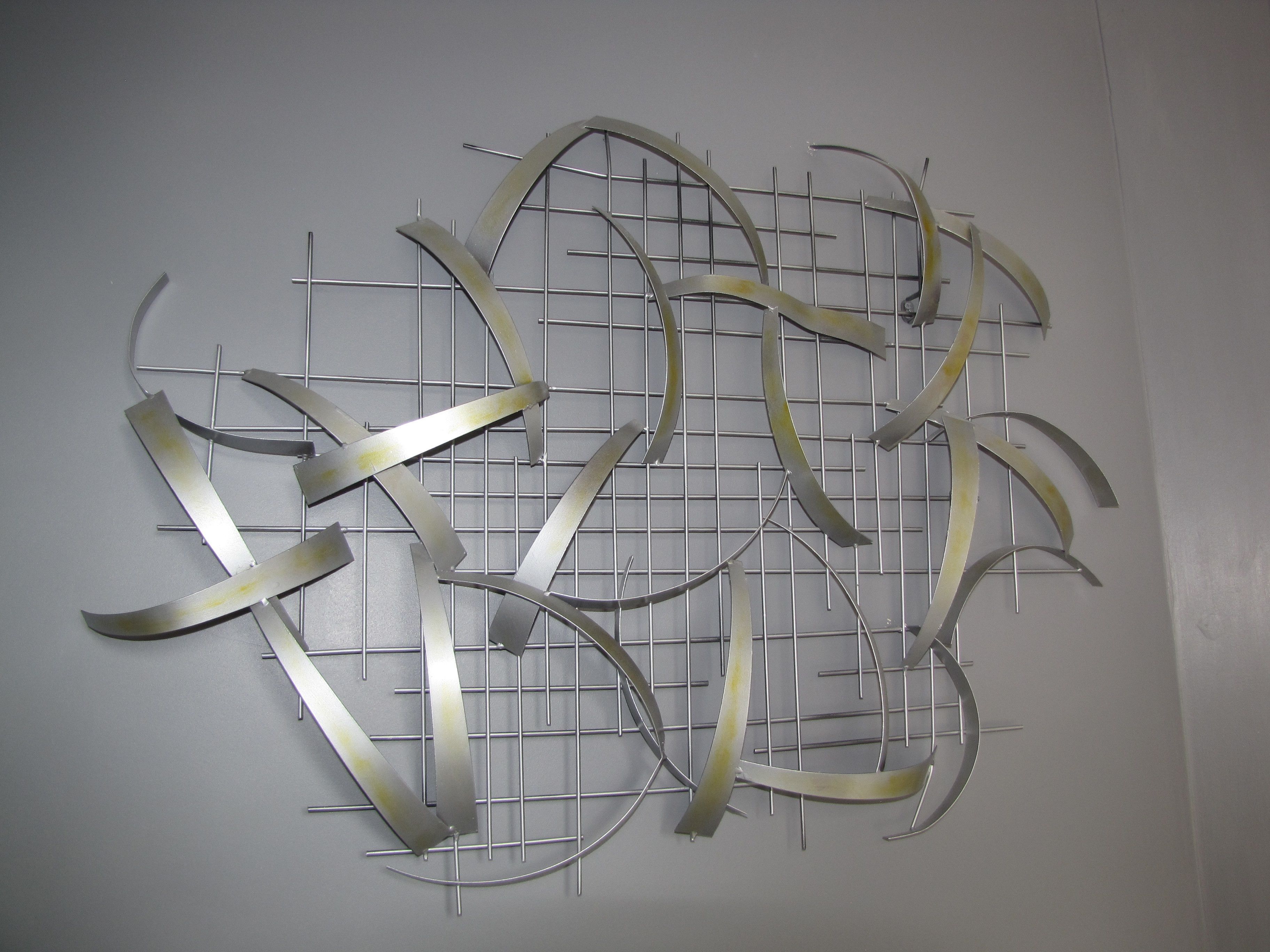 A metal sculpture with curved and straight elements arranged on a grid background.