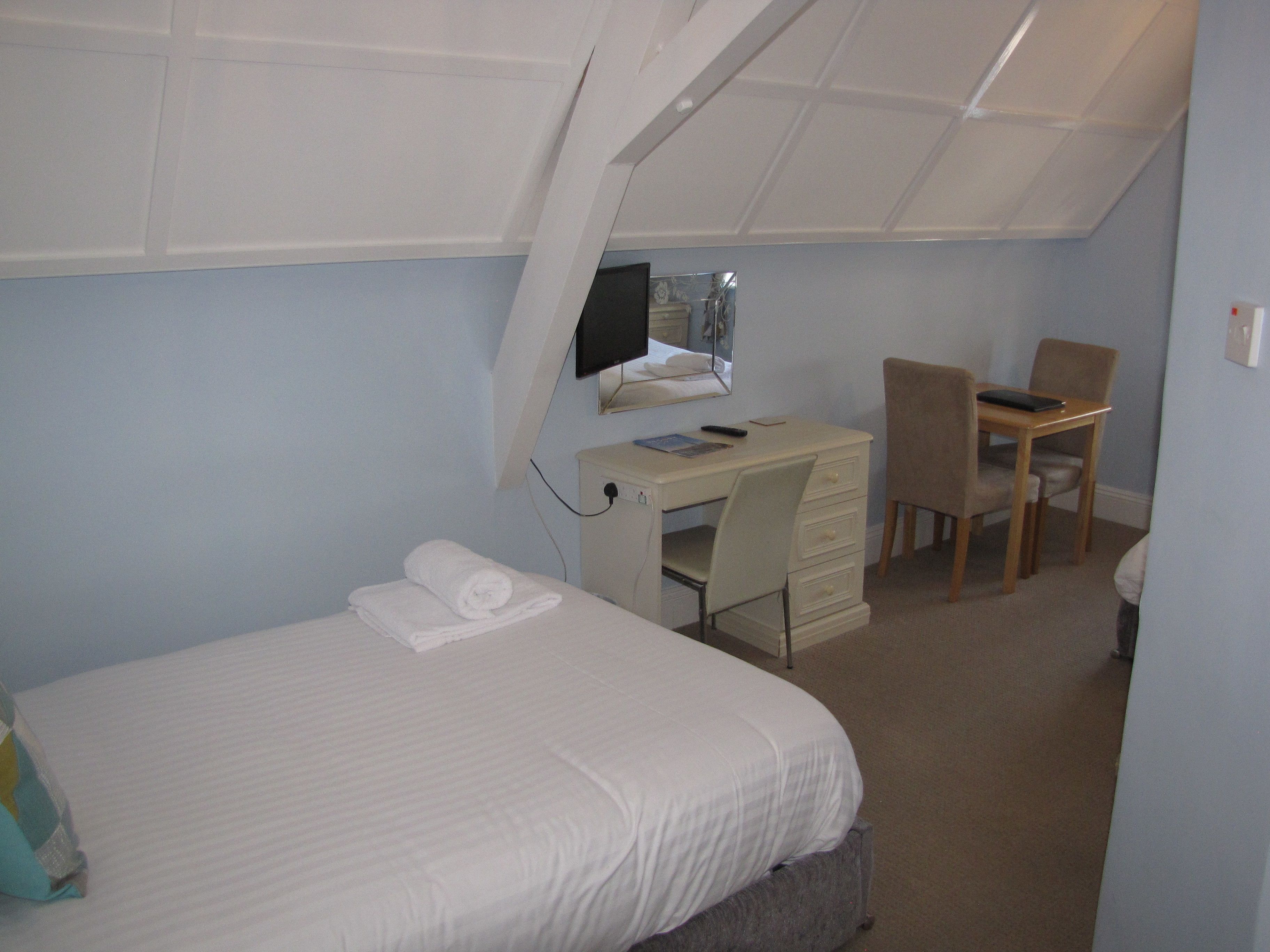 Un dormitorio con cama, escritorio, silla y monitor de ordenador.