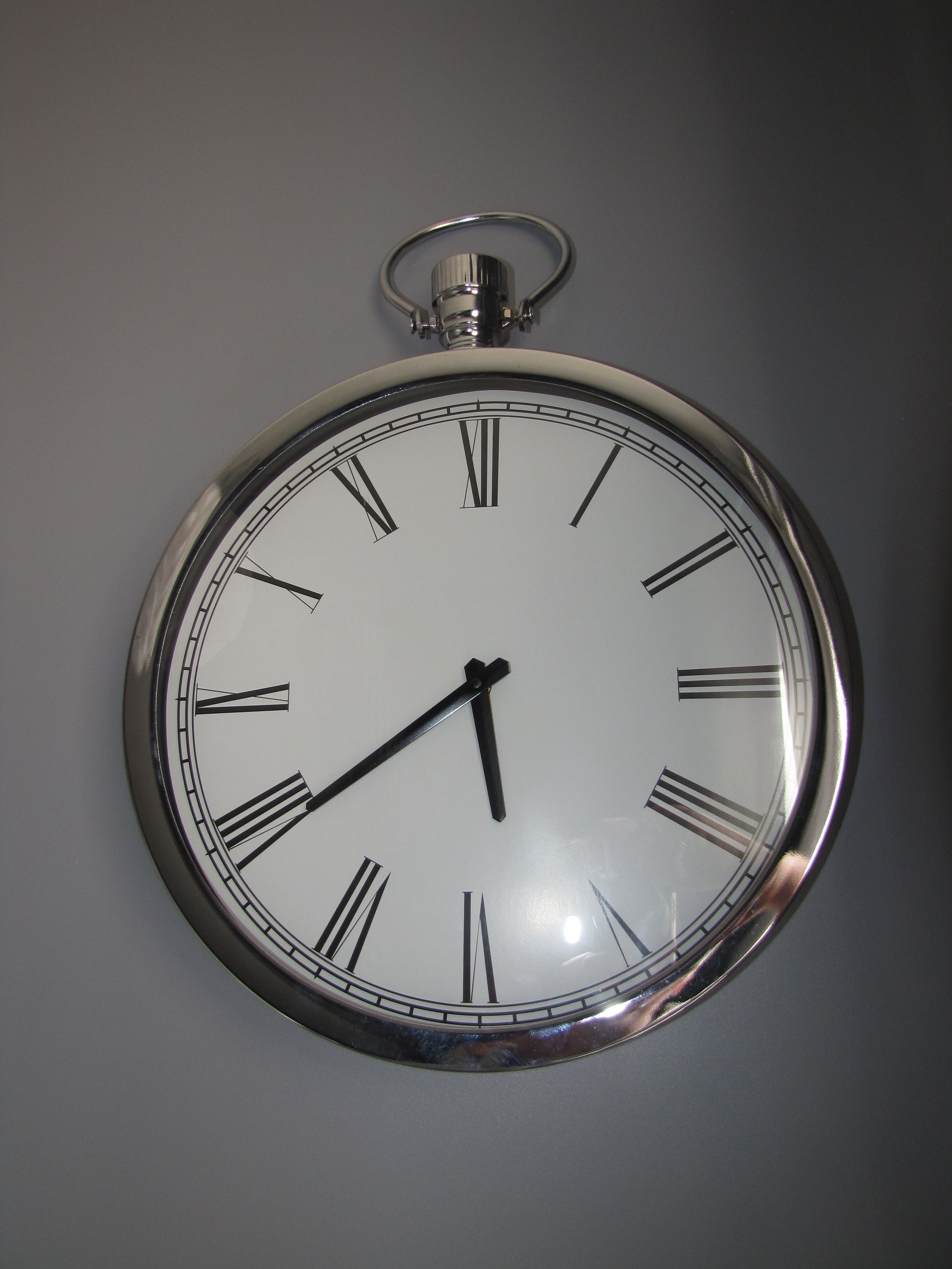 Un reloj de pared analógico con acabado metálico y números romanos.