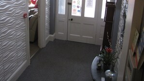 Un couloir avec un mur à texture, un lustre, une porte dotée de panneaux en verre dépoli et une petite table surmontée d’un vase.