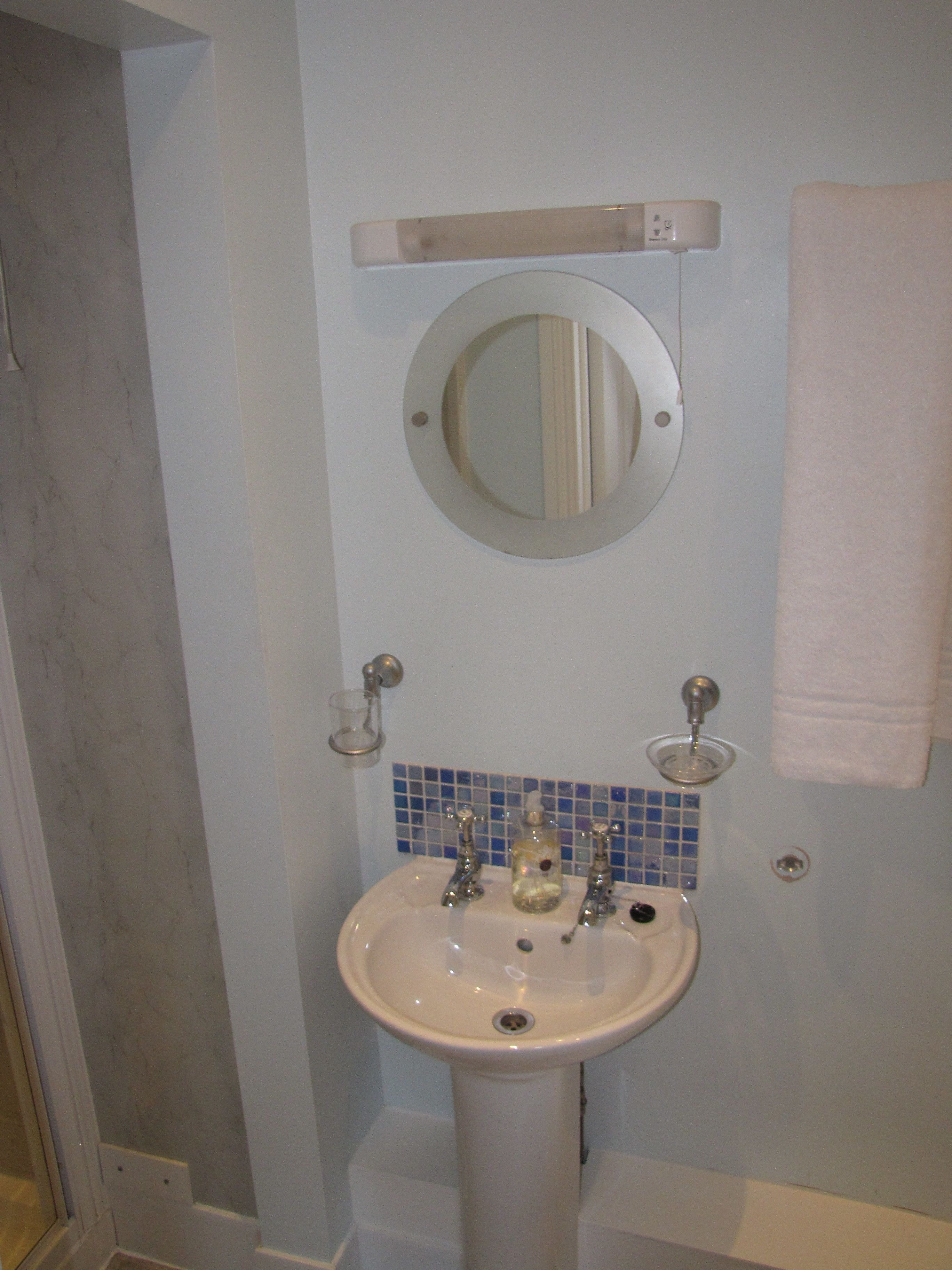 A bathroom with a white pedestal sink, a mirror above it, and a blue-tiled backsplash.