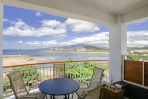 A balcony with a round table and chairs, overlooking a beach and a body of water with mountains in the distance. - Blue Sea Sunny Sea View Homestay (Checheng)