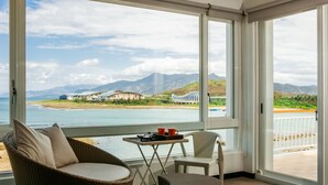 A balcony with wicker chairs, a small table with a tray, and a view of a coastal area with buildings and mountains. - Blue Sea Sunny Sea View Homestay (Checheng)
