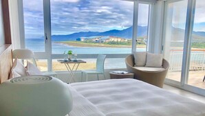 A bedroom with a large bed, a chair, a small table, and a view of the sea and mountains. - Blue Sea Sunny Sea View Homestay (Checheng)