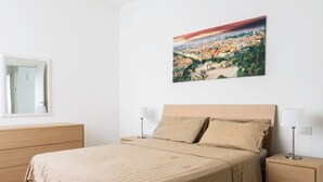 Une chambre à coucher avec un lit, deux tables de chevet, une commode, un miroir et un tableau représentant un paysage urbain accroché au mur.
