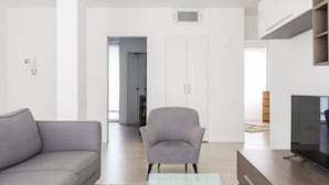 Un salon moderne avec un canapé gris, une table basse en verre et un téléviseur posé sur un meuble en bois.