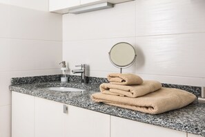 A bathroom with a granite countertop, a sink, a mirror, and a stack of beige towels.