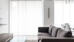 Un salon moderne avec un canapé gris, une table basse en verre et un mur blanc agrémenté d’une décoration minimaliste.