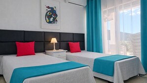 Habitación de hotel con dos camas, una mesita de noche con lámpara, una ventana con cortinas y un equipo de aire acondicionado.