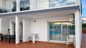 Un edificio moderno de dos pisos con balcón, ventanas amplias y un patio con mobiliario exterior.