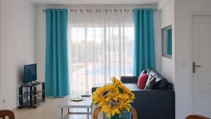 Una sala de estar con un sofá, una mesa de centro, un televisor y una ventana con cortinas.
