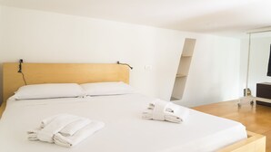 A hotel room with a wooden headboard, a large bed with white linens, and a wooden nightstand with a lamp.