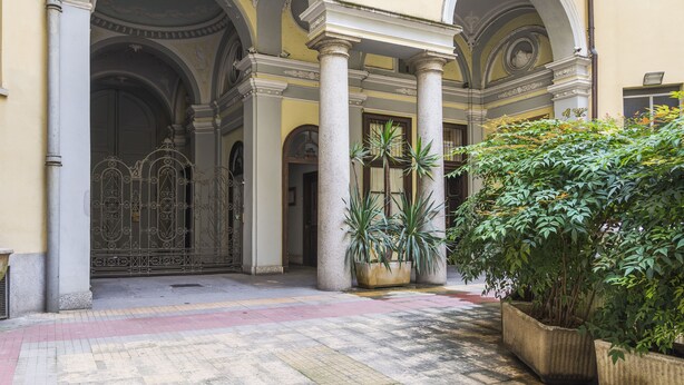 A courtyard with a large metal gate, columns, and potted plants.