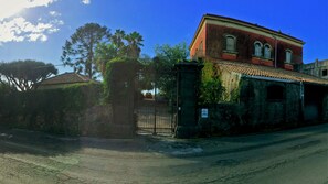 A building with a red facade, a tiled roof, and a gated entrance. - Malvarosa (Giarre)