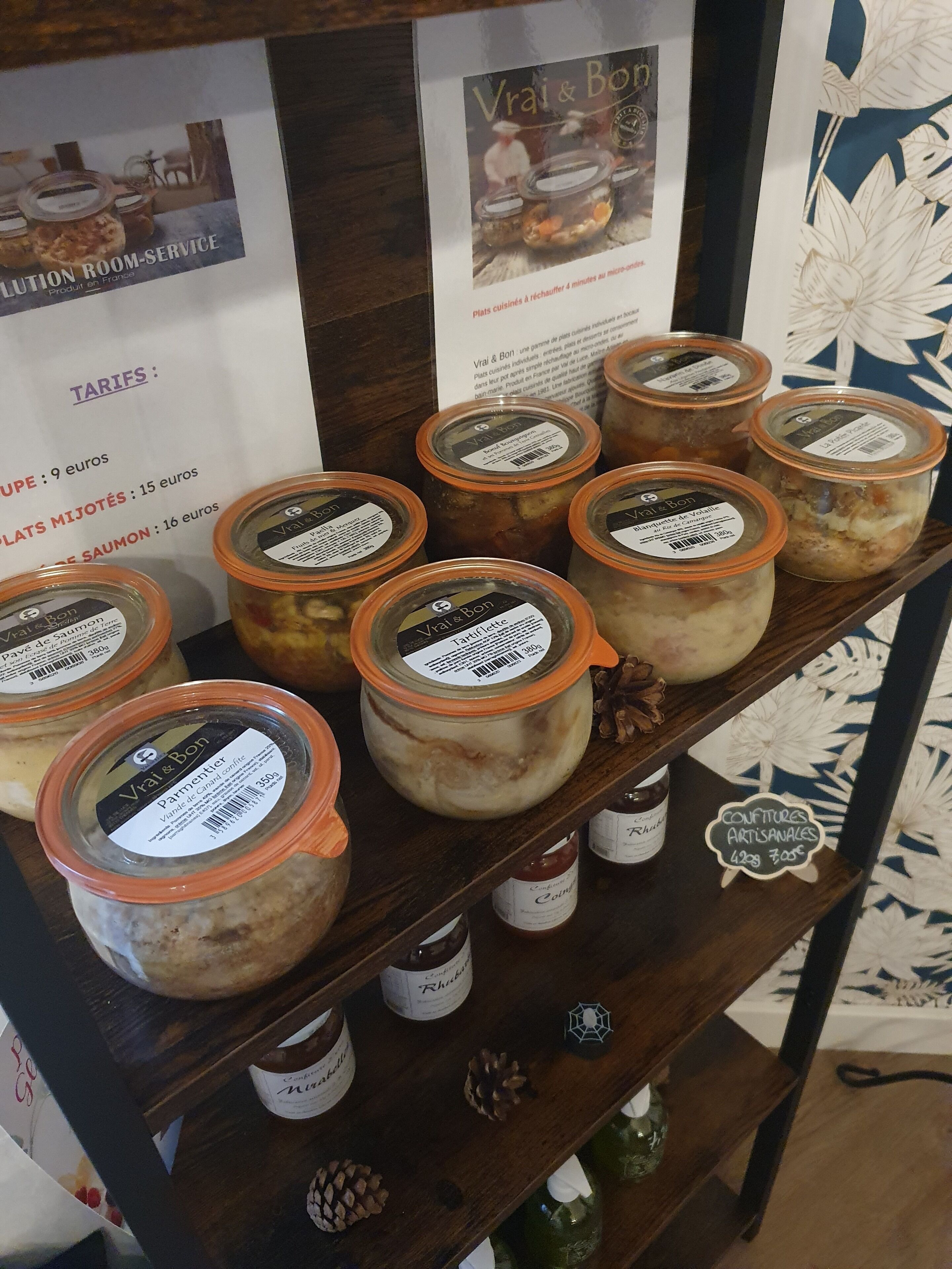 Un estante con frascos de alimentos en conserva, un cartel con tarifas y una pared decorativa con motivos florales.
