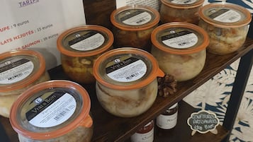 Un estante con frascos de alimentos en conserva, un cartel con tarifas y una pared decorativa con motivos florales.