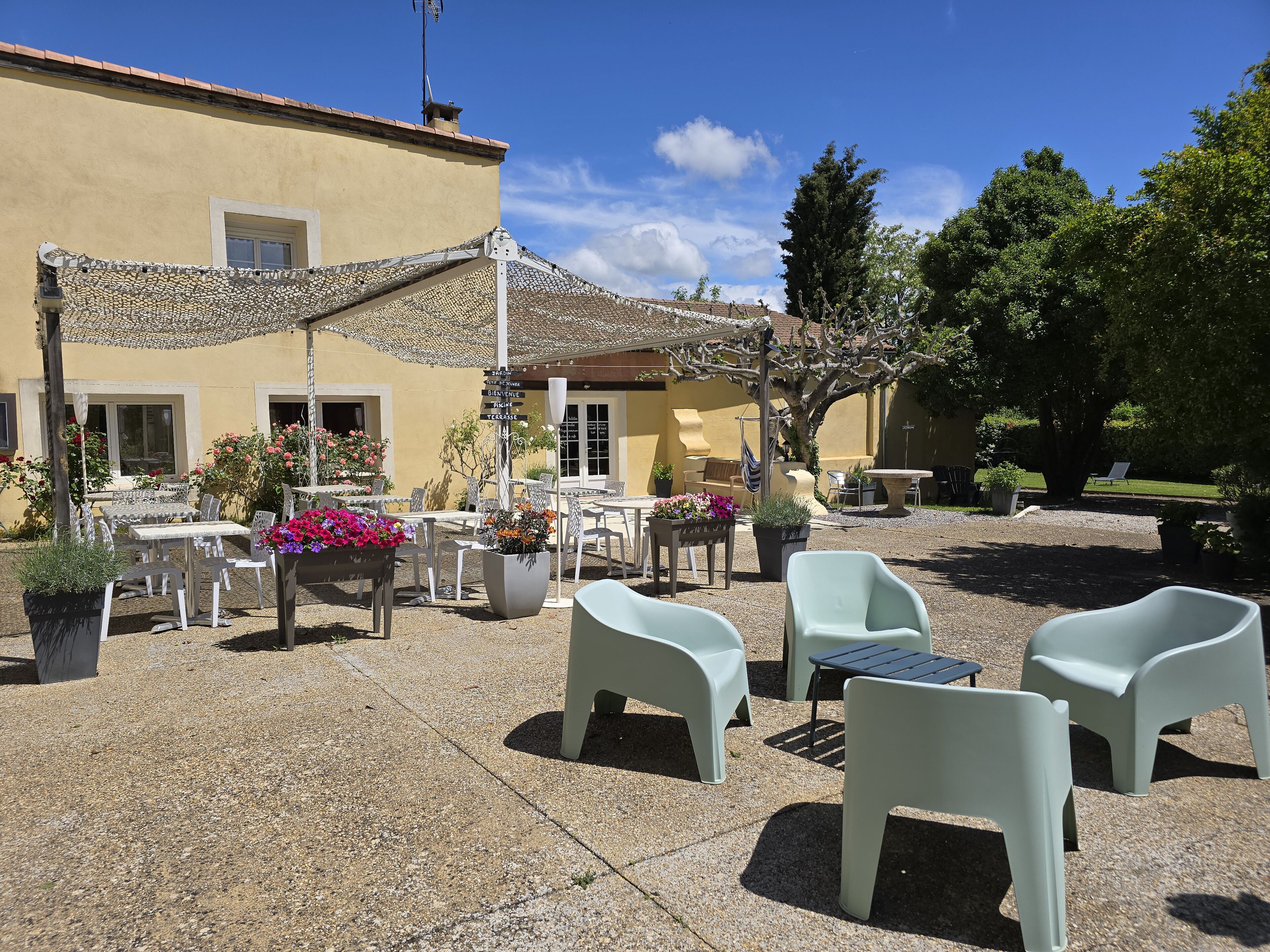 An outdoor patio with stone flooring, white plastic chairs, and potted plants.